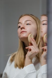 Woman applying make-up in front of mirrored cabinet