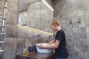 blonde boy using bathroom with lit LED mirrored cabinet